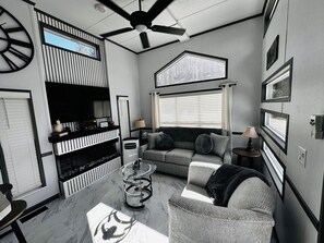 Ein modernes Wohnzimmer mit Flachbildfernseher, Deckenventilator, Sofa, Couchtisch und Kamin.