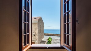 Vista a través de una ventana abierta de un edificio de piedra con tejado de tejas, cielo despejado y un cuerpo de agua.