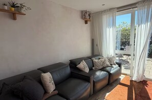 A living room with a sofa set, a small shelf with plants, and a sliding glass door to the outside. - Spacious and Cozy House for Rent - Sleeps 6 - East London (London)