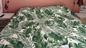 A bed with a tropical leaf pattern bedspread, a bedside table with a lamp, and a wall-mounted power outlet.