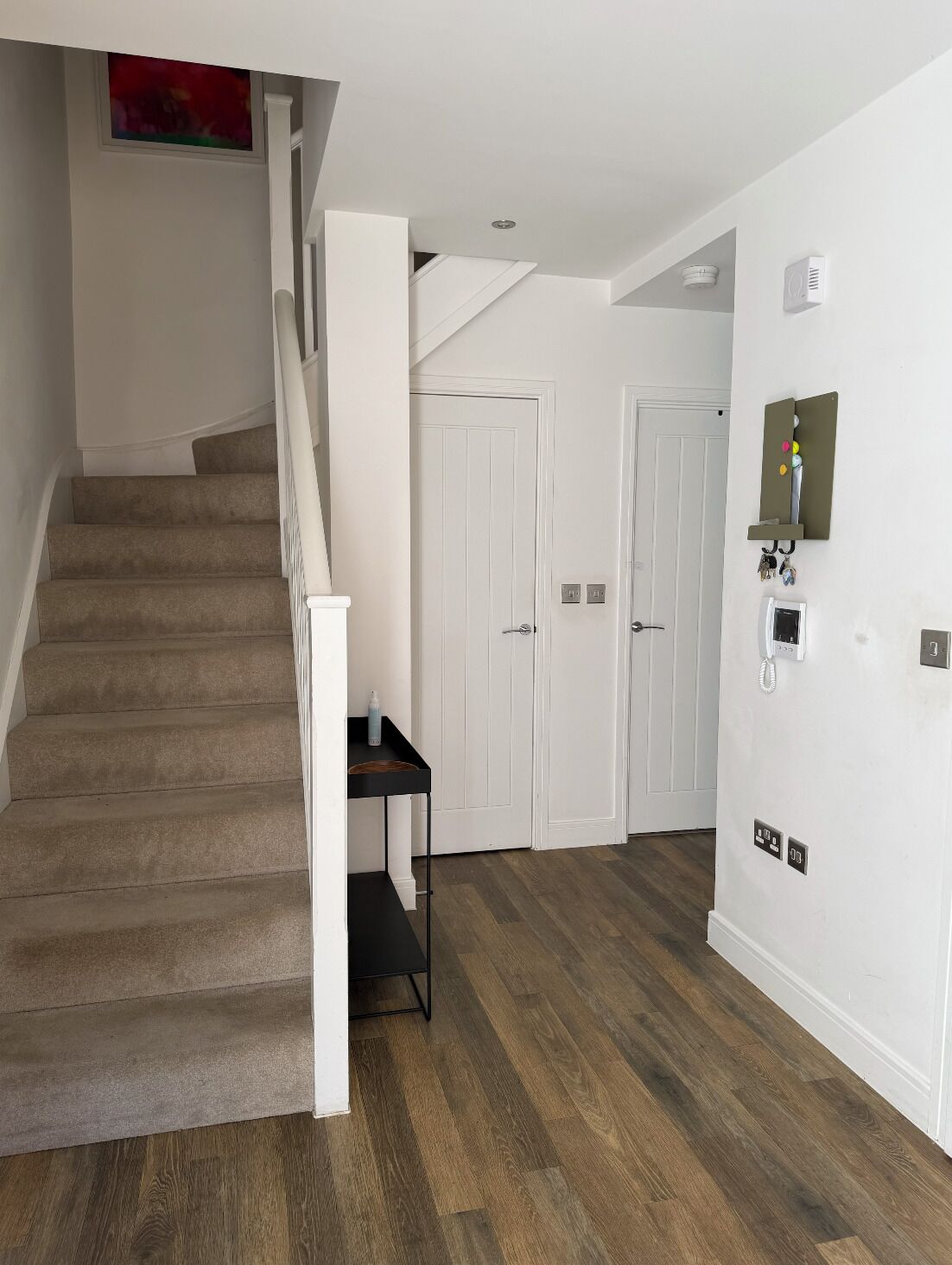 A staircase with carpeted steps, a small table with a bottle, and a wall-mounted phone.