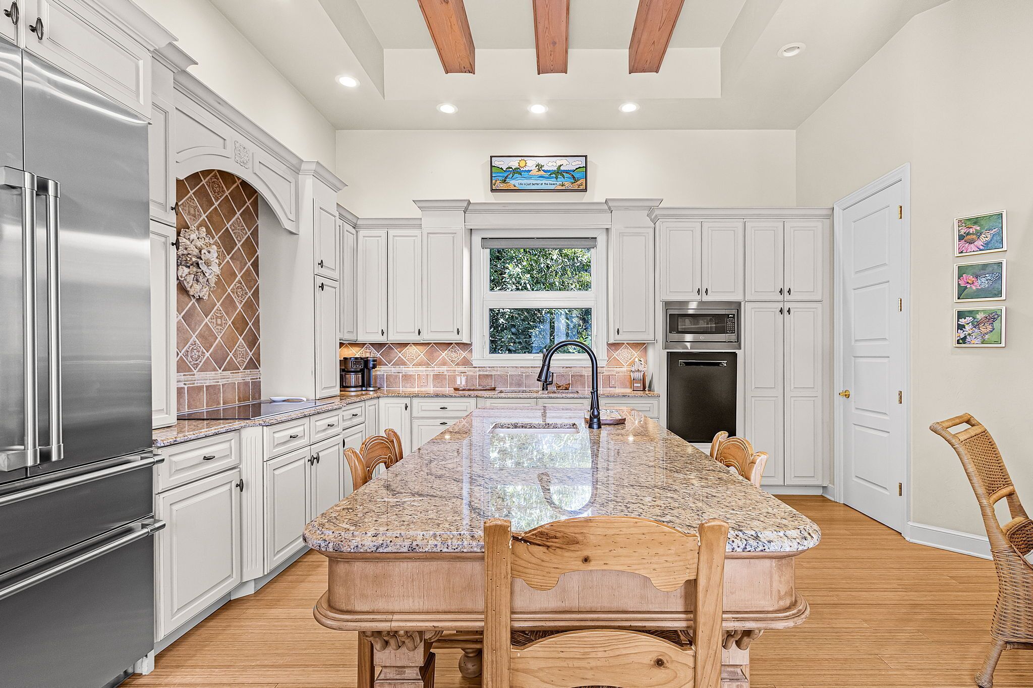 A kitchen with white cabinetry, a granite countertop island, stainless steel appliances, and a window with a view of greenery.