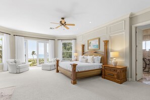 A spacious bedroom with a large bed, a sitting area with a chair, and a view of the outdoors. - 5 Bedroom / 5 Bath Luxury Estate (Captiva)