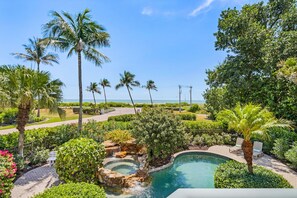 A pool area with a hot tub, surrounded by lush greenery and palm trees, overlooking a beach. - 5 Bedroom / 5 Bath Luxury Estate (Captiva)