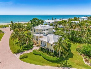 A multi-story residential building with a landscaped garden, palm trees, and a view of the ocean. - 5 Bedroom / 5 Bath Luxury Estate (Captiva)