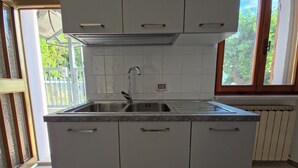 Cocina con alacenas blancas, pileta de acero inoxidable y ventana con vista a vegetación.