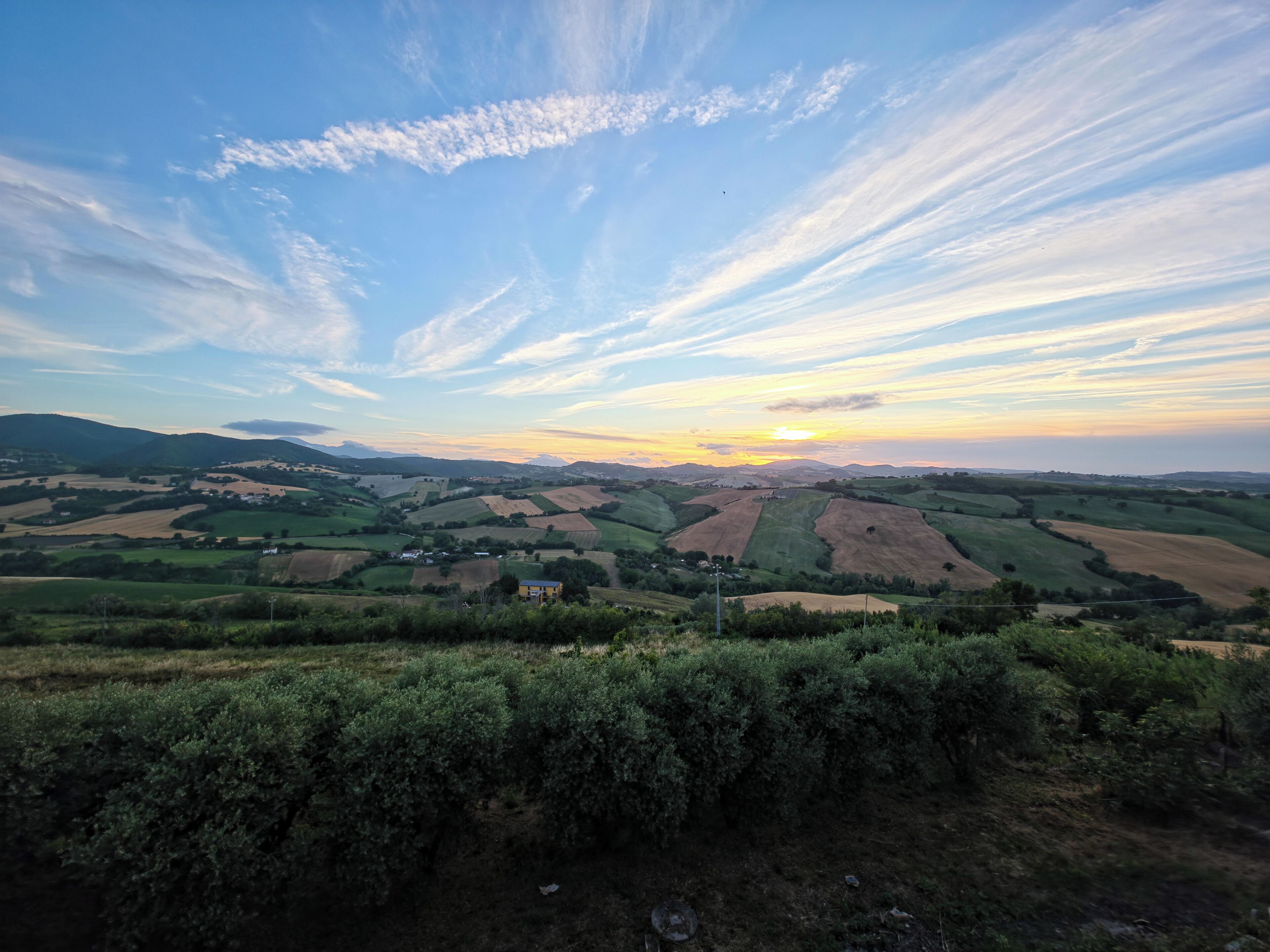 Un paysage rural avec des collines douces, des champs et un petit bâtiment au premier plan.