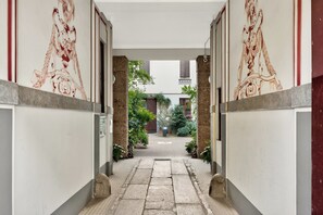 A corridor with a tiled floor leading to a courtyard with plants and a building in the background. - Isola Stay - A beautiful little nest in Isola, in the heart of Milan (Milano)