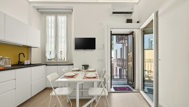 A modern kitchen with white cabinets, a dining table set for four, and a TV mounted on the wall. - Isola Stay - A beautiful little nest in Isola, in the heart of Milan (Milano)