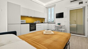 A compact hotel room with a bed, kitchenette, and a TV. - Isola Stay - A beautiful little nest in Isola, in the heart of Milan (Milano)