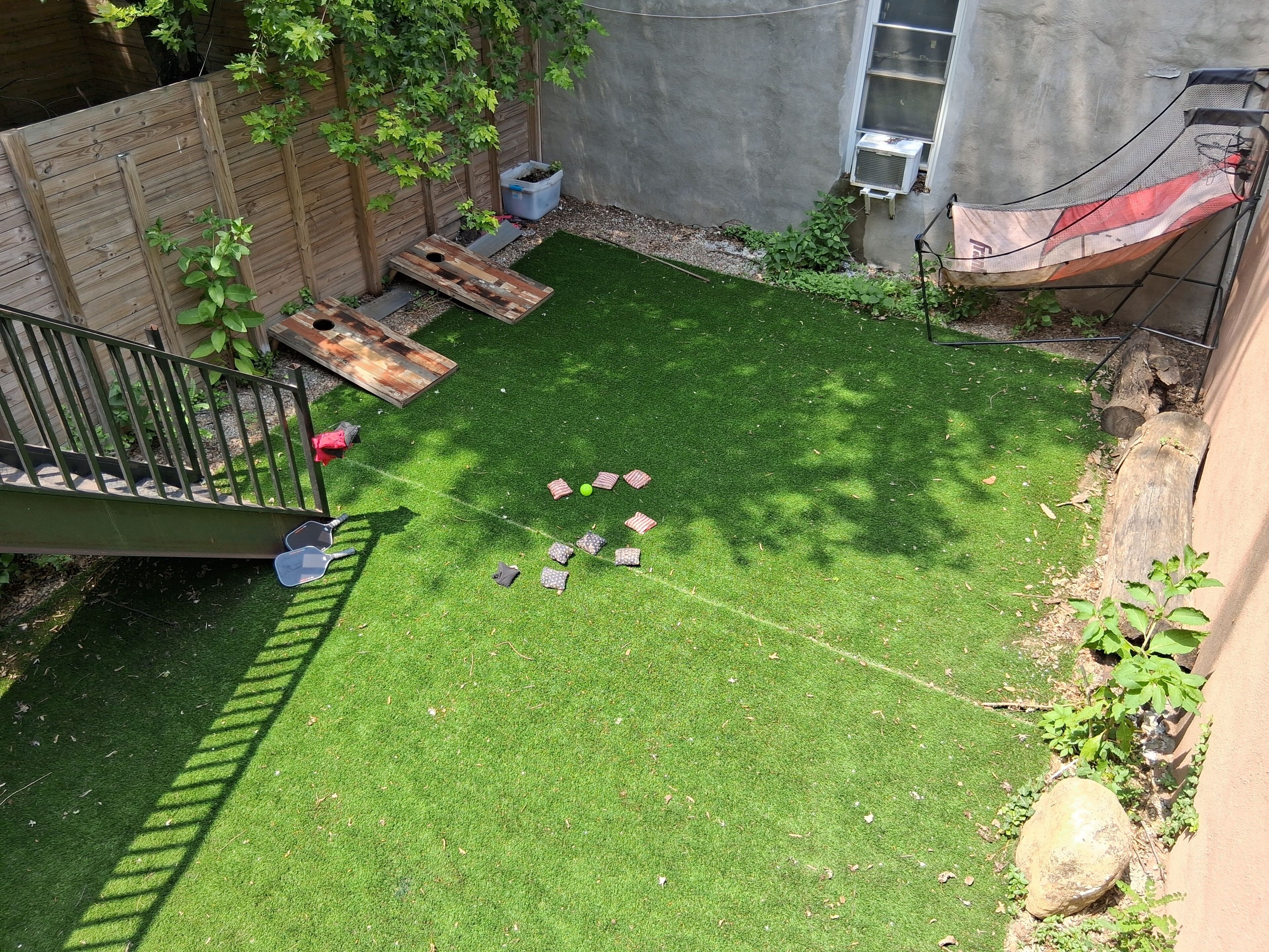 A backyard with artificial grass, a wooden fence, a wooden deck, and a small garden area.