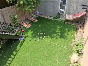 A backyard with artificial grass, a wooden fence, a wooden deck, and a small garden area.