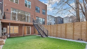A modern two-story building with a balcony, a wooden fence, and a well-maintained lawn. - New 2-bedroom Garden apartment in peaceful Brooklyn with AC and charm (Brooklyn)