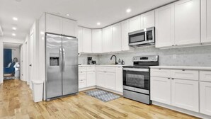 A modern kitchen with white cabinets, stainless steel appliances, and a wooden floor. - New 2-bedroom Garden apartment in peaceful Brooklyn with AC and charm (Brooklyn)
