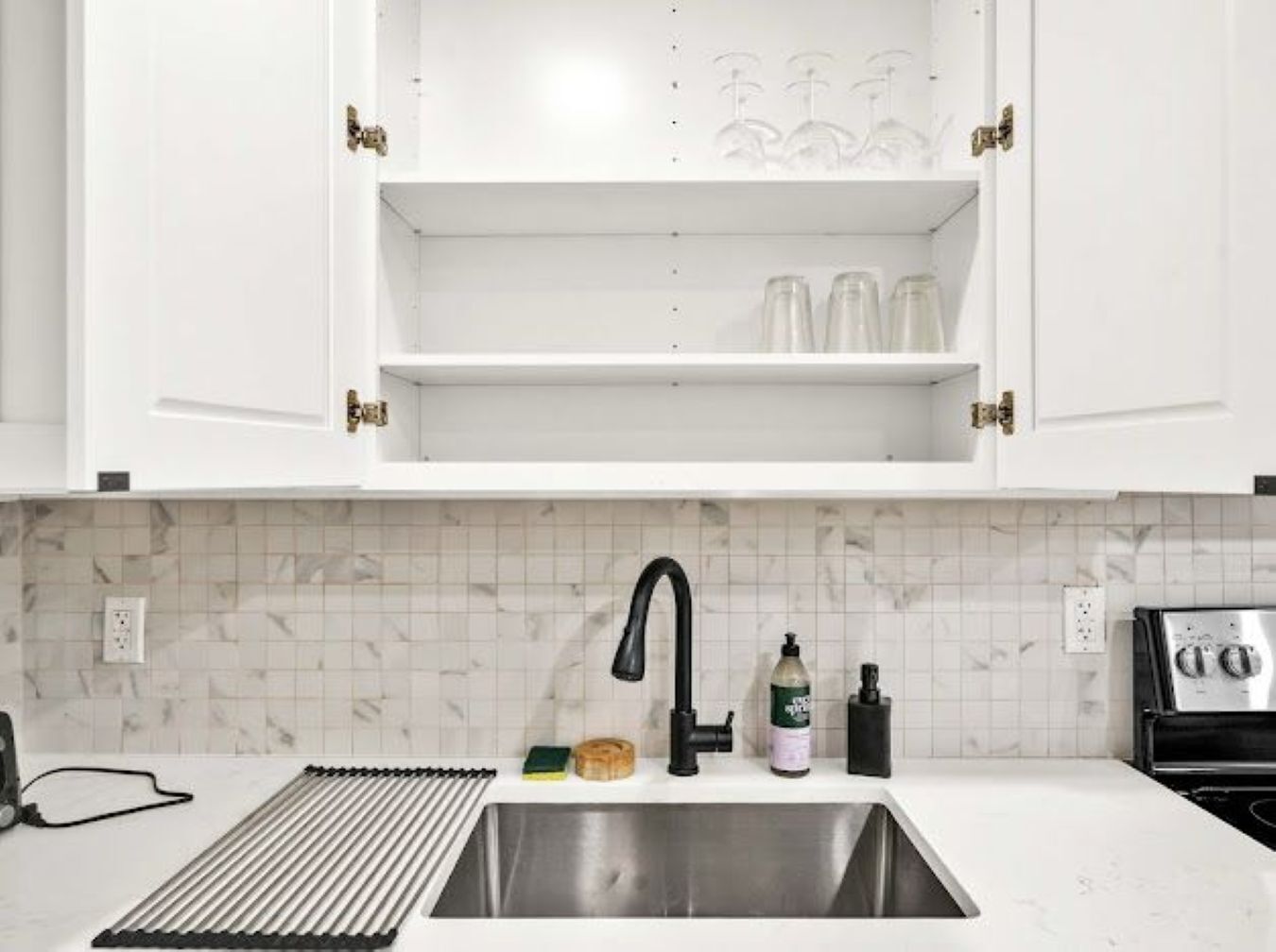 A kitchen with white cabinets, a stainless steel sink, a black faucet, a tiled backsplash, and a toaster.