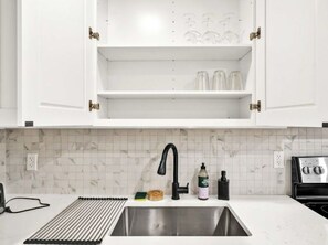 A kitchen with white cabinets, a stainless steel sink, a black faucet, a tiled backsplash, and a toaster.