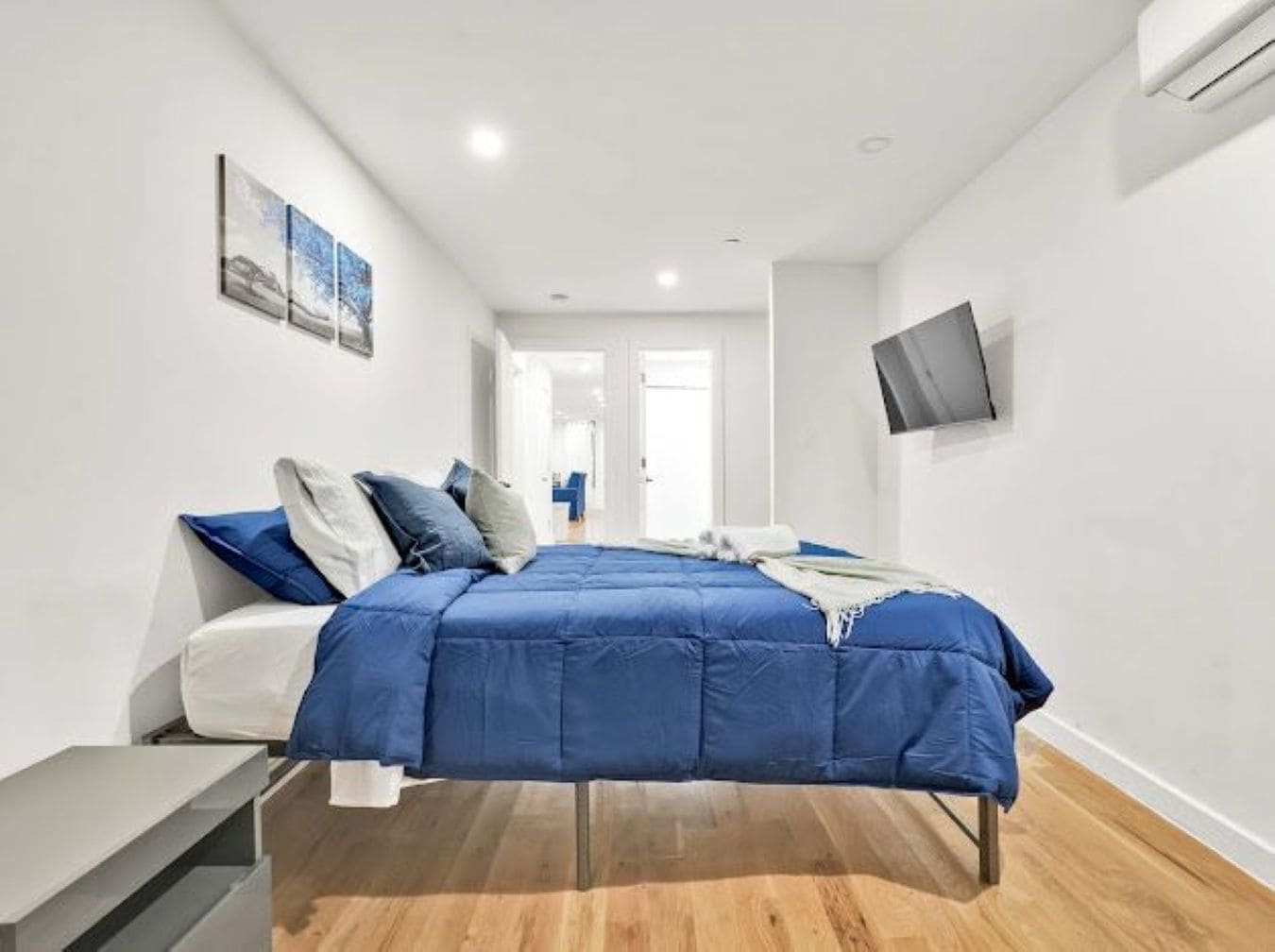 A modern bedroom with a bed, bedside tables, a flat-screen TV, and a hallway leading to a door.