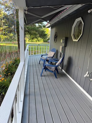 A covered porch with two blue chairs, a white railing, and a view of a green lawn. - Charming 3-bedroom house with in Boyne City (Boyne City)