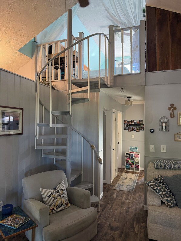 Ein mehrgeschossiges Interieur mit einer Wendeltreppe, einem Sofa mit einem 'Welcome to the Lake'-Kissen und einer Aufbewahrungseinheit für 'Beach towels'.