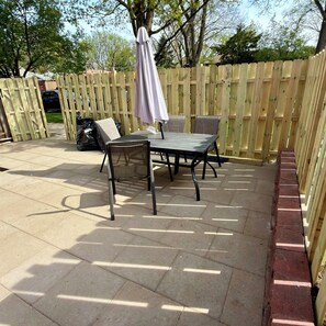 Un patio al aire libre con mesa y sillas, cercado por una valla de madera y con una zona cubierta.