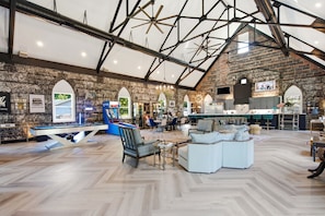A spacious indoor area with a high ceiling, exposed brick walls, and a pool table.