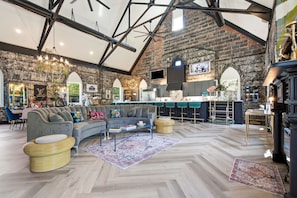A spacious interior with a high ceiling, exposed brick walls, a modern kitchen, and a seating area with a sofa and ottoman.