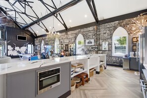 A modern kitchen with a central island, built-in oven, and a stone wall backdrop.