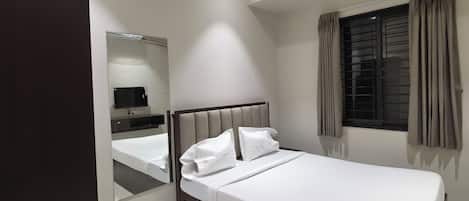 A modern bedroom with a bed, a mirror, a window with curtains, and a ceiling light.