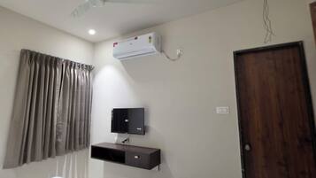 Habitación de hotel con cama, aire acondicionado de pared, televisor, puerta de madera y ventilador de techo.