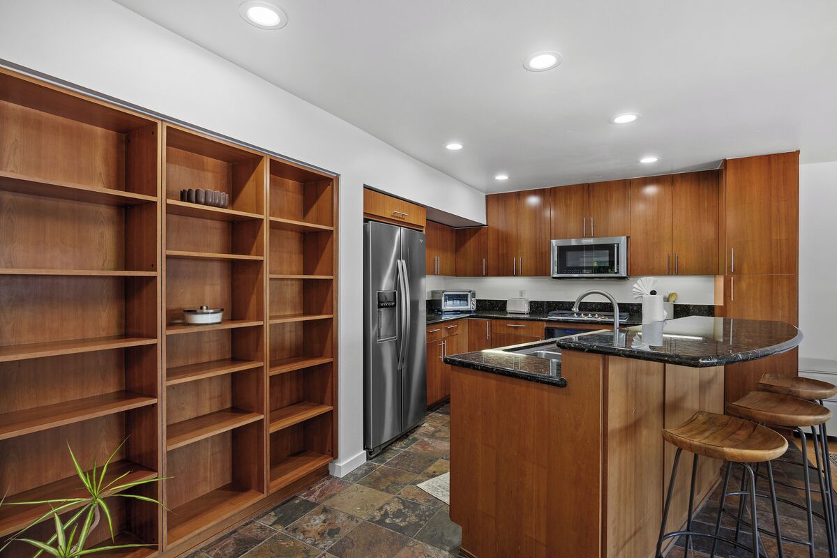 A modern kitchen with wooden cabinets, a stainless steel refrigerator, a microwave, and a bar stool area.
