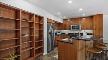 A modern kitchen with wooden cabinets, a stainless steel refrigerator, a microwave, and a bar stool area.