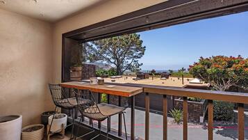 A balcony with a view of a building and trees, two bar stools, and a table.