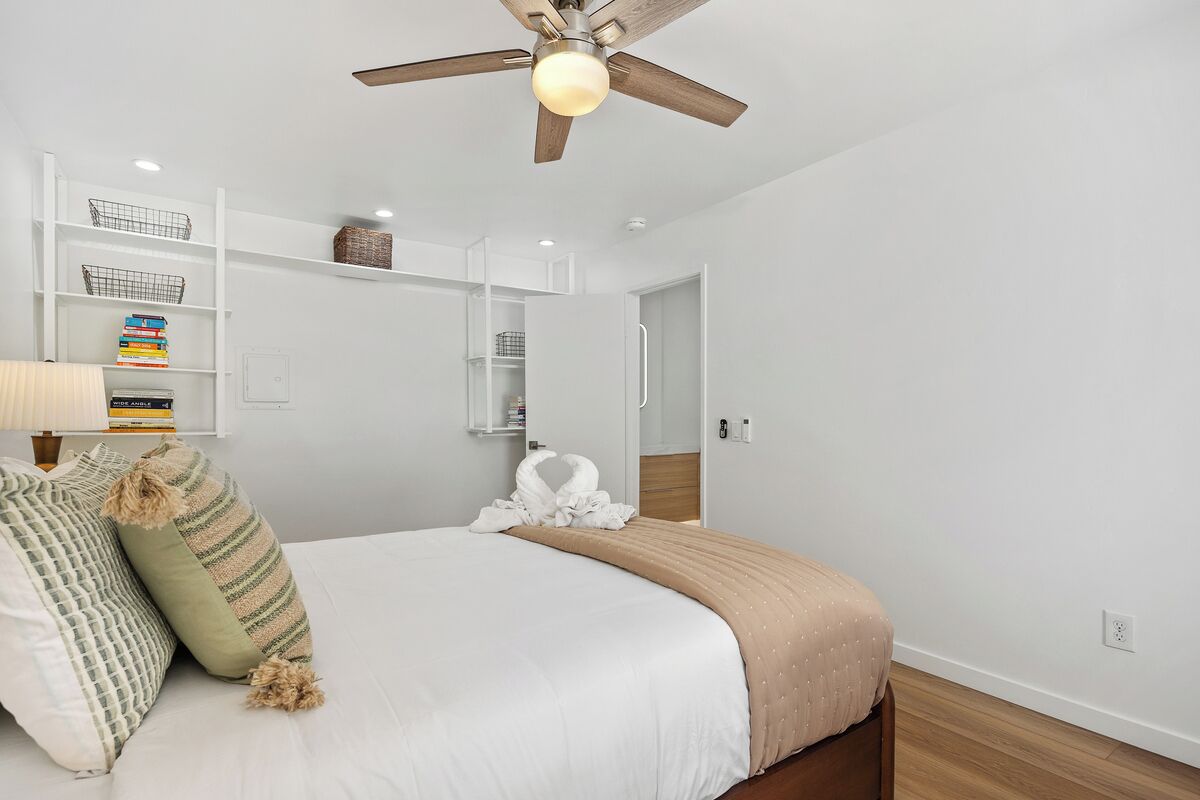Un dormitorio con cama, almohadas, ventilador de techo, mesita de noche y estantería.