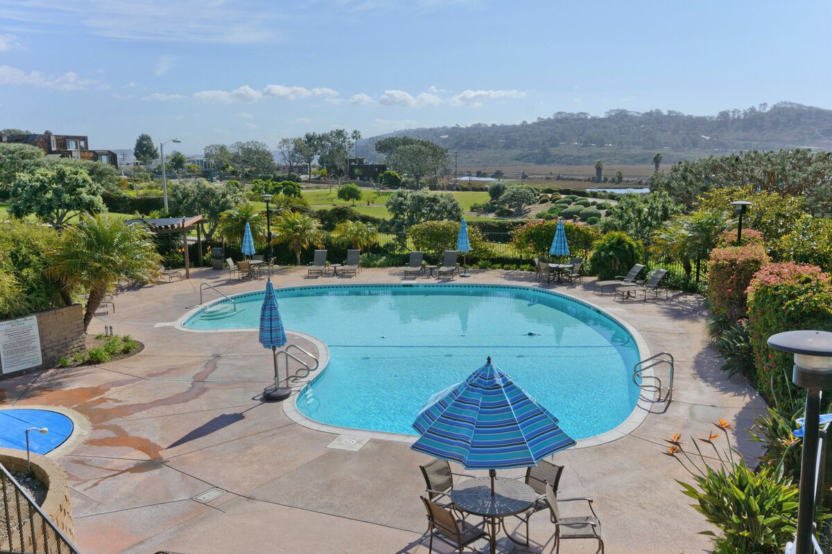 A swimming pool with lounge chairs and umbrellas, surrounded by landscaped gardens and a view of distant hills.