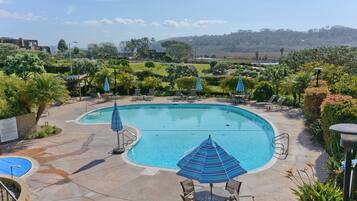 A swimming pool with lounge chairs and umbrellas, surrounded by landscaped gardens and a view of distant hills.