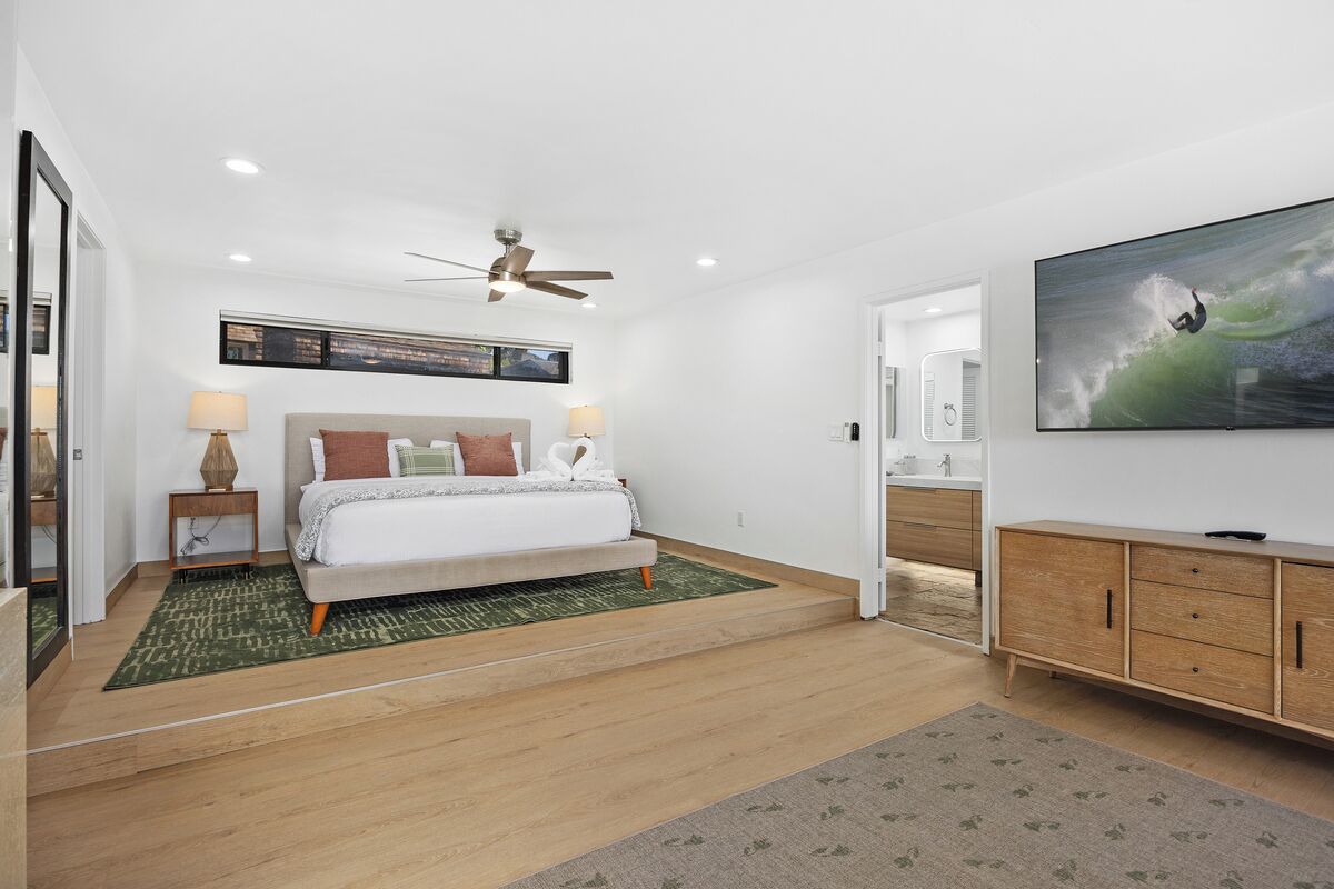 A modern bedroom with a bed, a ceiling fan, a TV, and a large window.