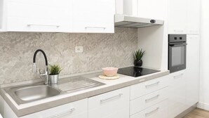 A modern kitchen with a stainless steel sink, white cabinets, a built-in oven, and a backsplash with a floral pattern. - IMB23 • Central Apartment in Milan • (Milano)