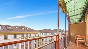 Een balkon met uitzicht op omliggende gebouwen, een metalen hekwerk en twee stoelen.
