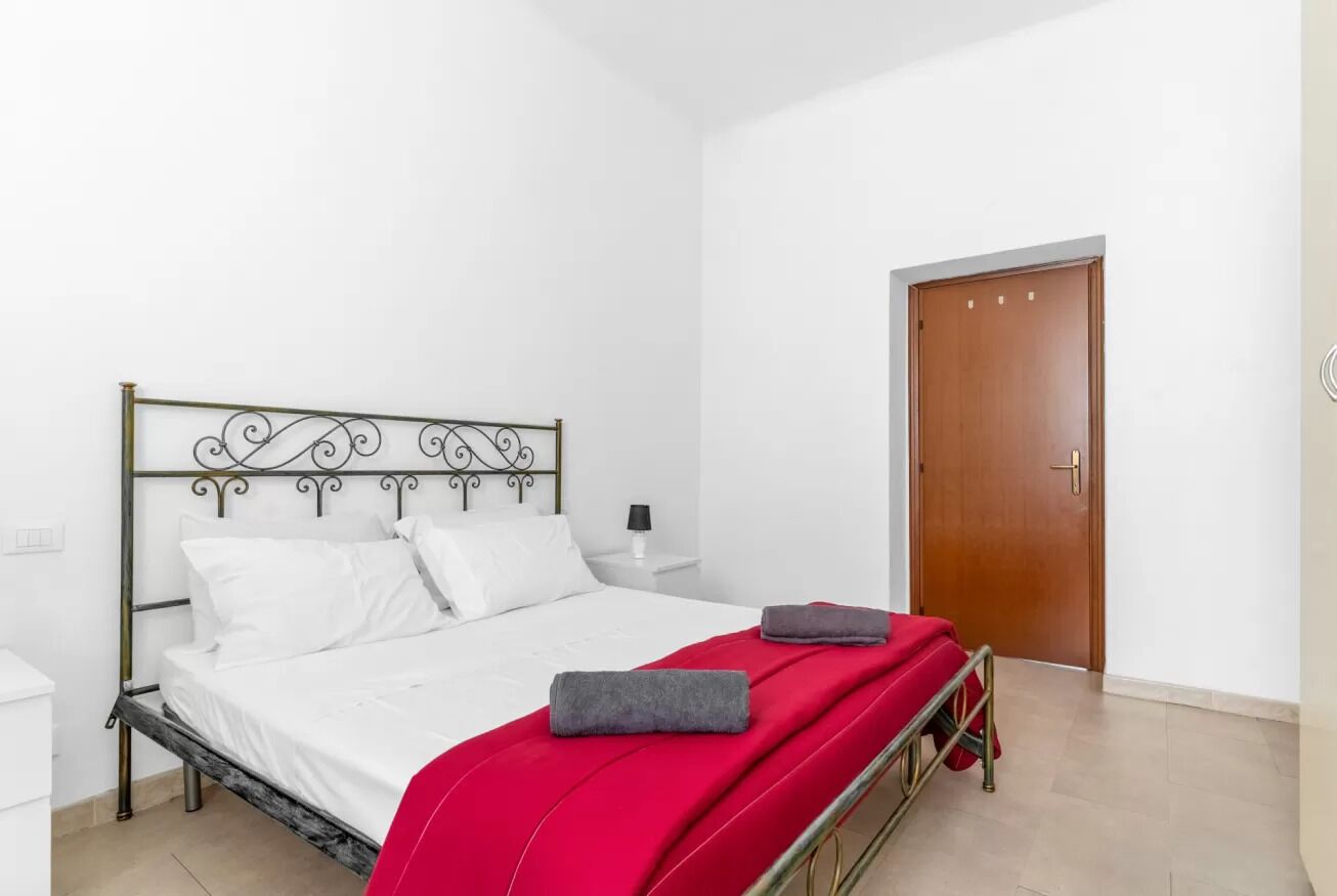 Un lit simple avec un cadre en métal, des draps blancs et une couverture rouge.