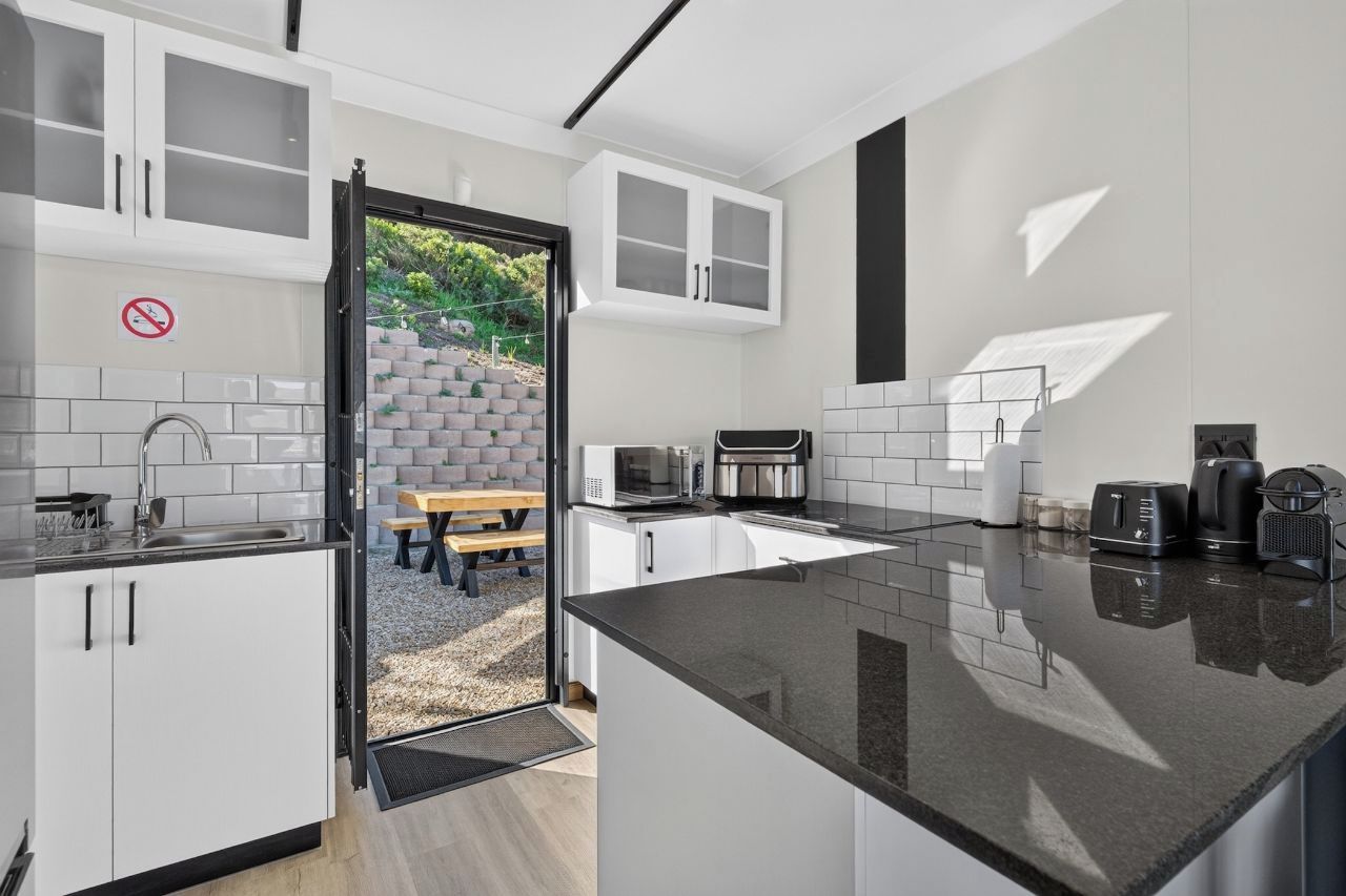 Une cuisine moderne avec des meubles blancs, un plan de travail noir et une vue sur un espace patio aménagé avec une table et des chaises.