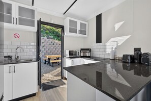 A modern kitchen with white cabinets, a black countertop, and a view of a patio area with a table and chairs. - Stunning sea view cottage (Cape Town)