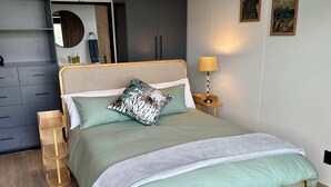 Um quarto bem arrumado com cama, mesa de cabeceira, abajur e um espelho.