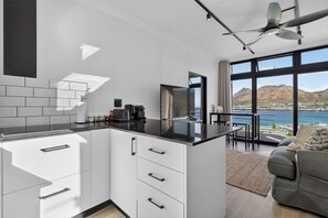 A modern kitchen with white cabinets and a black countertop, a dining area with a view of the sea, and a gray sofa. - Stunning sea view cottage (Cape Town)