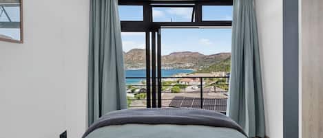 A bedroom with a large bed, a view of the sea, and a balcony with solar panels.