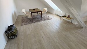 A spacious loft with a high ceiling, a skylight, a wooden floor, a small table, and a chair.