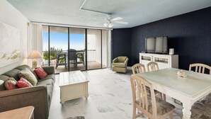 A living room with a sofa, coffee table, dining table, chairs, a TV, and a ceiling fan. - Includes Xplorie Activities & Linens. PYRAMID-1BR OF condo w/outdoor pool. (Ocean City)