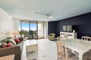 A living room with a sofa, coffee table, dining table, chairs, a TV, and a ceiling fan. - Includes Xplorie Activities & Linens. PYRAMID-1BR OF condo w/outdoor pool. (Ocean City)