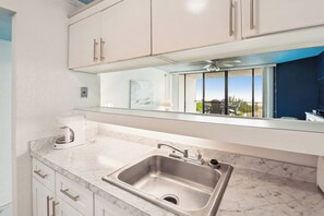 A modern kitchen with a stainless steel sink, white cabinets, and a large window offering a view of the outdoors. - Includes Xplorie Activities & Linens. PYRAMID-1BR OF condo w/outdoor pool. (Ocean City)