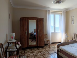 A hotel room with a bed, a wooden wardrobe, a table with a pitcher, a chair, and a window with curtains. - First floor of a village house, 15 minutes from the sea (Sari D Orcino)