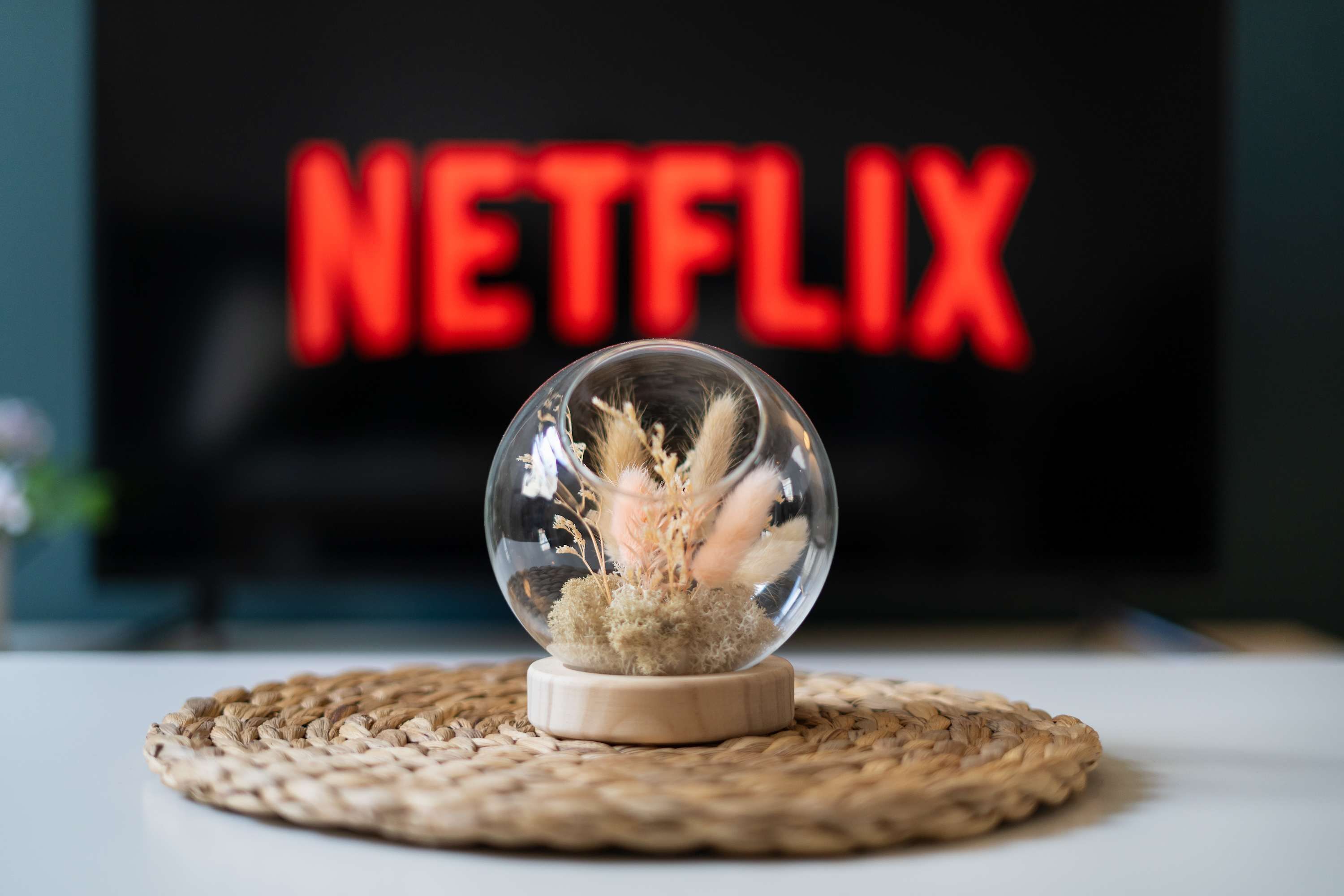 A clear glass sphere with dried plants on a woven placemat, placed in front of a television displaying the word 'NETFLIX' in red letters.